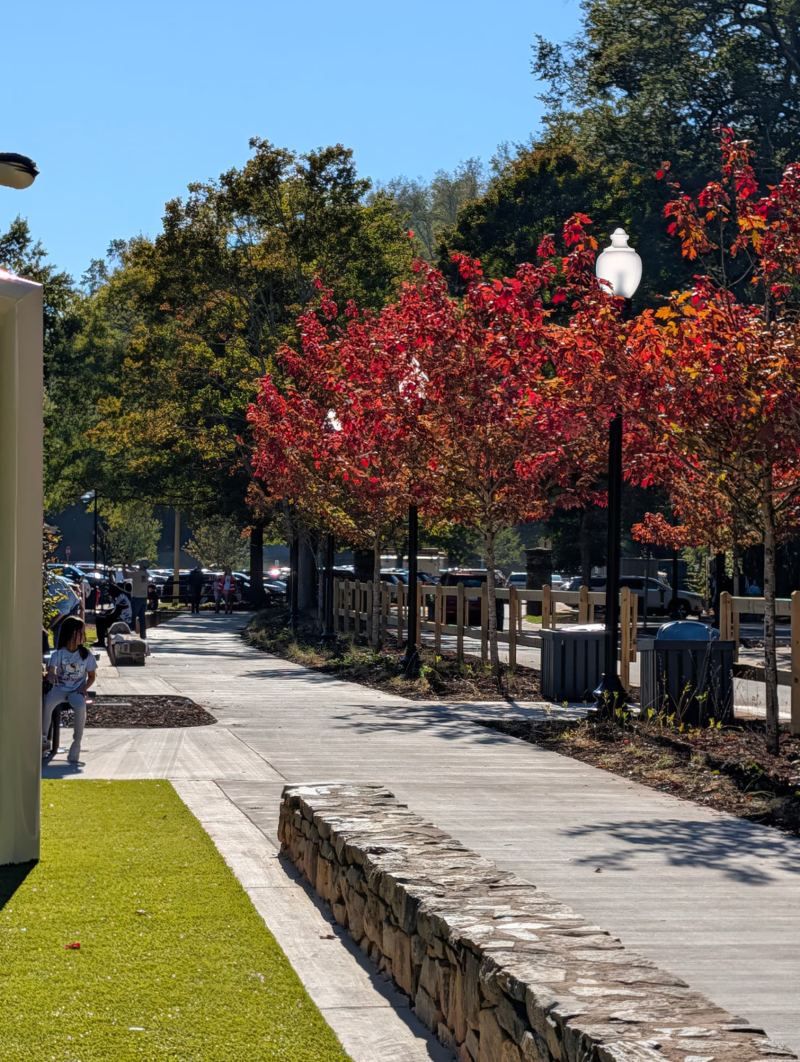 A paved walkway at Cleveland Park Playground, with red autumn trees, benches, lamps and a low stone wall.