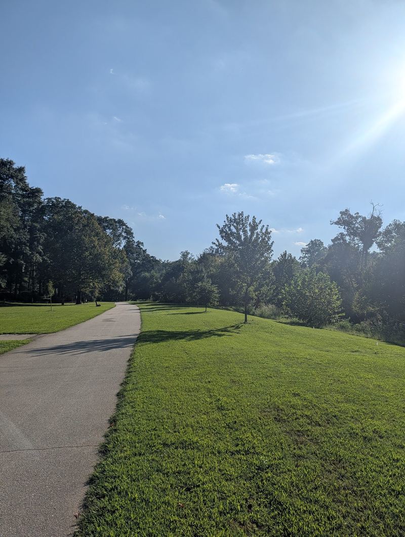 A paved path running beside a wide, sloping lawn toward trees.